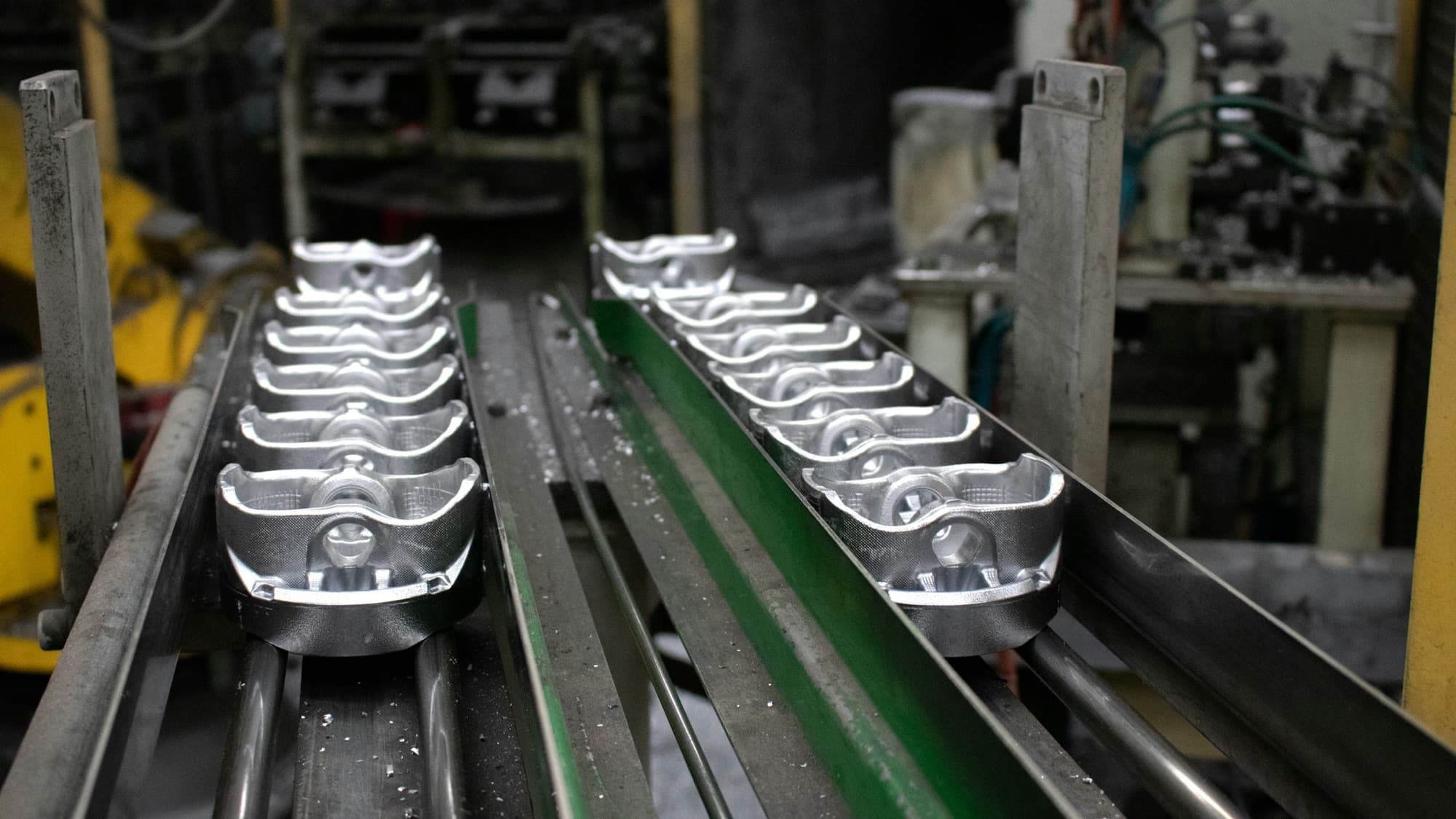 Freshly cast aluminum parts queued on a conveyor rail beside the casting cell