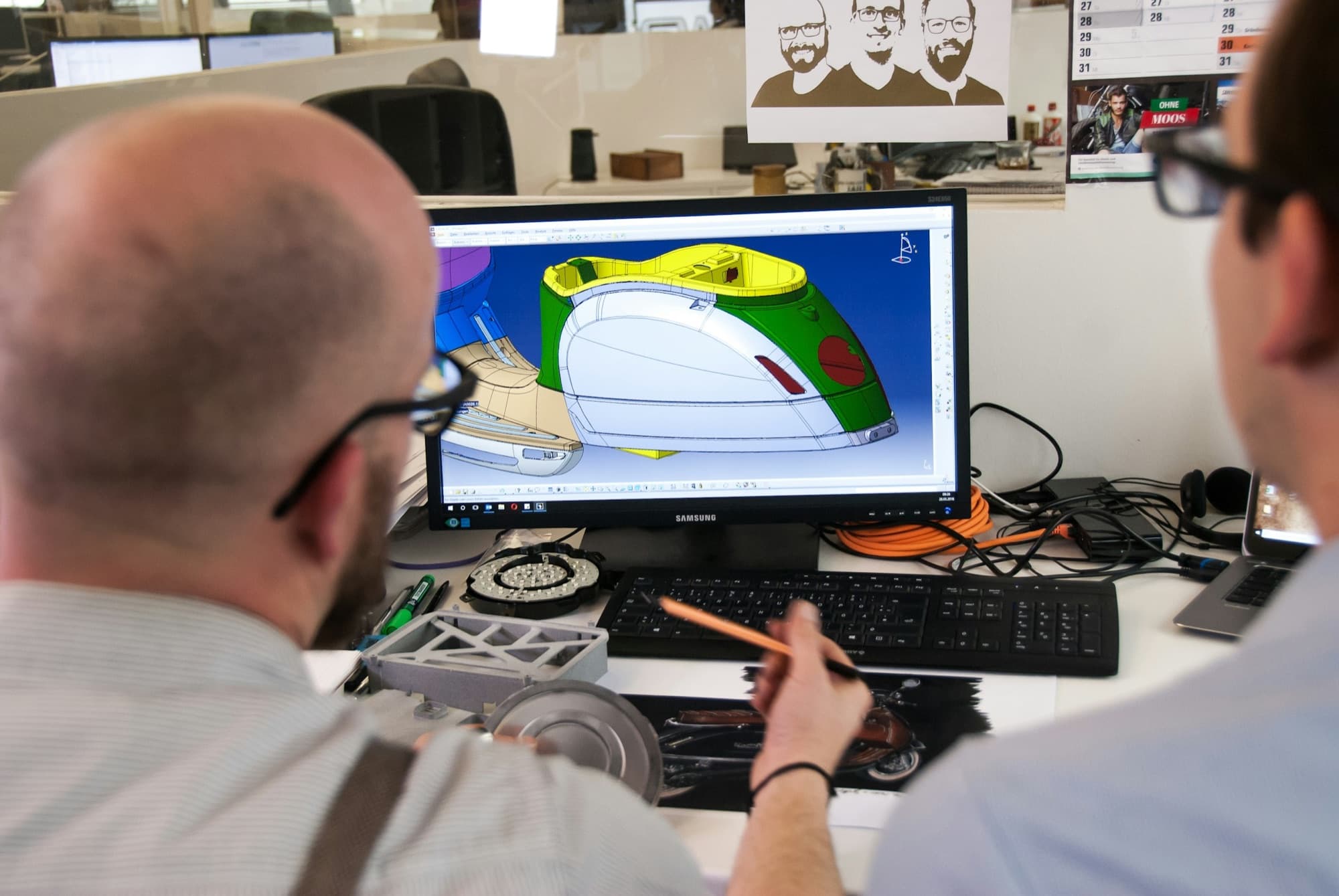 Two engineers review a 3D CAD model of a molded body panel next to physical prototype parts