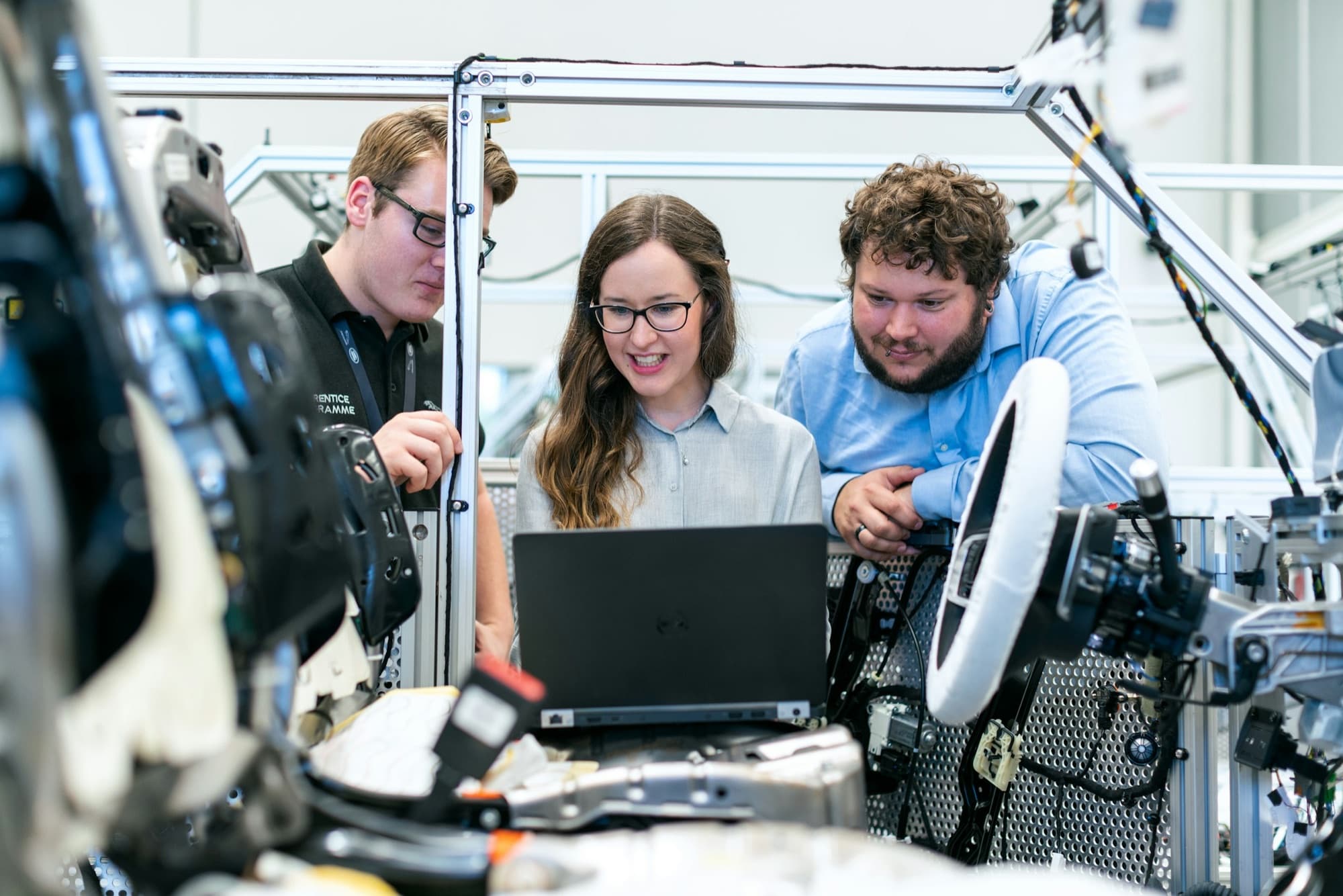 Three engineers review results on a laptop inside an automotive assembly test rig